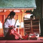 woman playing bamboo wind instrument in front of percussion instrument